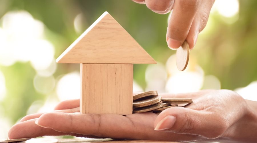 Χέρι γυναίκας με σπίτι και νομίσματα